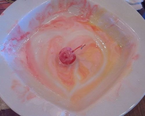 plate of eaten icecream, with melted icecream drawn heart and one cocktail cherry in the middle